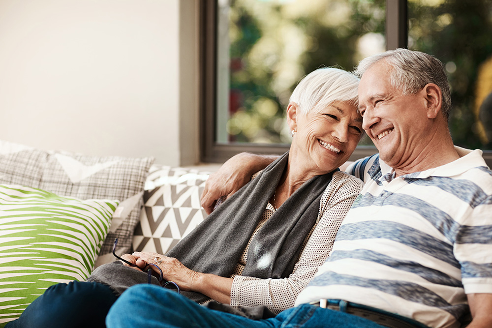 Smiling older couple sitting on an outdoor couch on a patio.