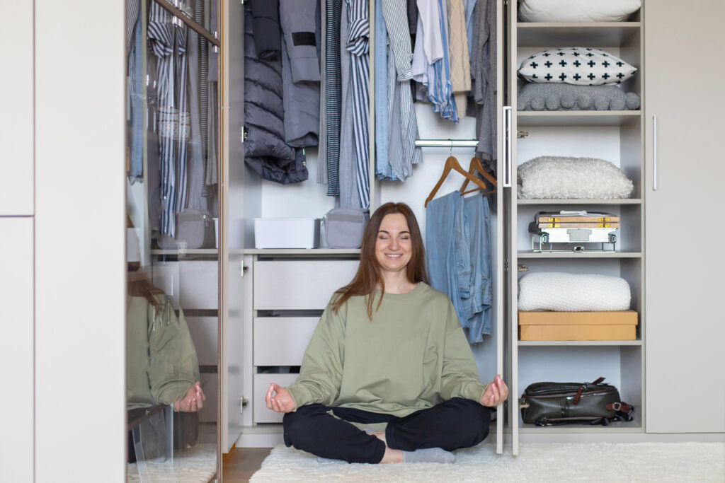 National Get Organized Month. Smiling woman in a happy yoga pose in front of a very organized closet.