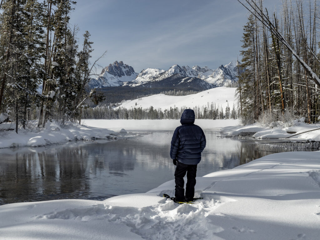 Winter snowshoer take a break along a riverside in winter to enjoy the view of the Idaho Sawtooth mountains