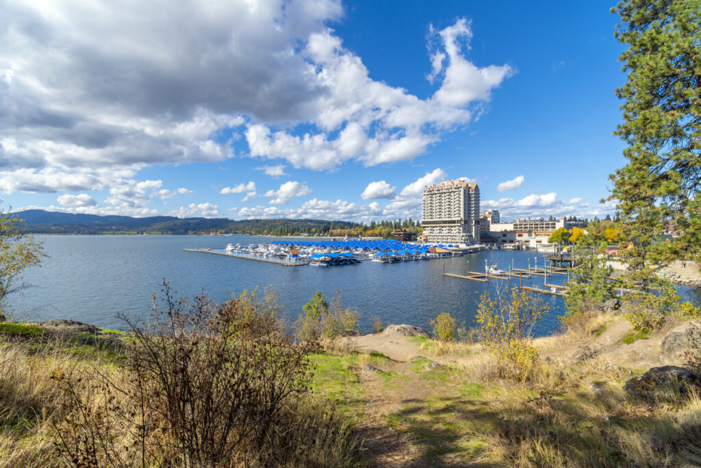 View from a small lakeshore beach on Tubbs Hill, a public park with walking trails, of the lake, marina, city beach and boardwalk at Coeur d'Alene, Idaho USA on a summer day. Coeur d’Alene is a city in northwest Idaho. It’s known for water sports on Lake Coeur d’Alene, plus trails in the Canfield Mountain Natural Area and Coeur d’Alene National Forest. McEuen Park offers a grassy lawn and a trailhead for adjacent Tubbs Hill. The lakeside City Park & Beach includes picnic areas and a playground. The Museum of North Idaho traces regional history, including the city's former timber industry.