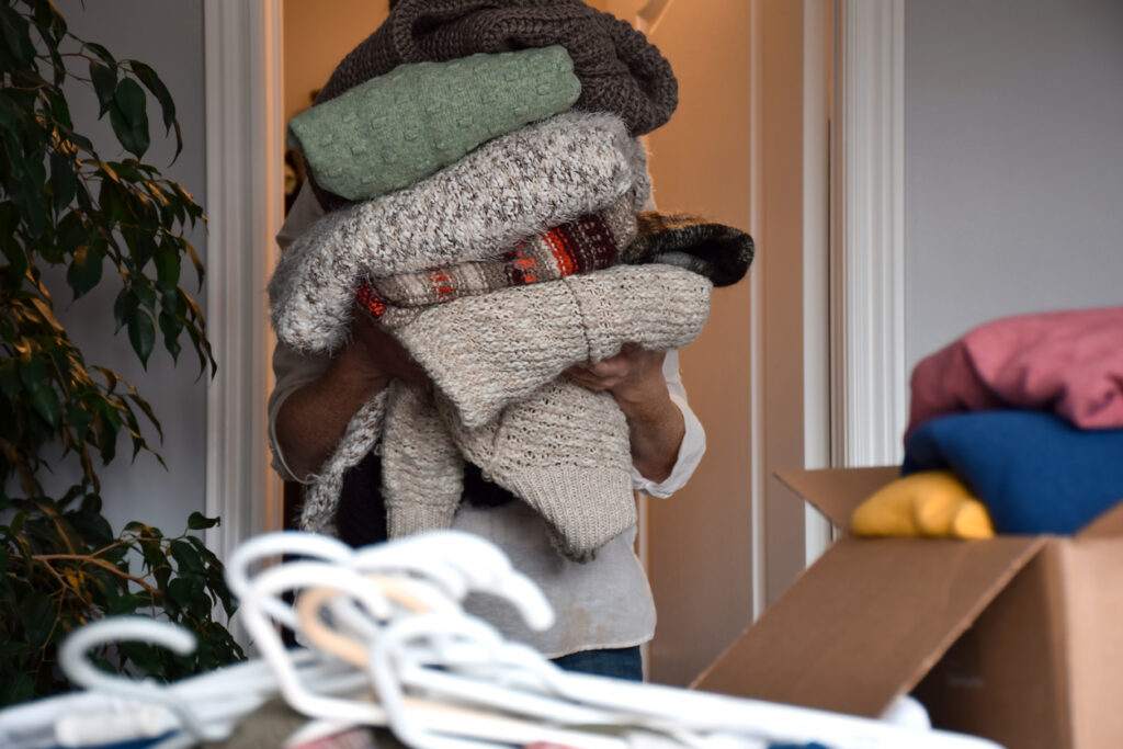 Woman holding a huge stack of winter knit sweaters, organizing and sorting clothes in her closet