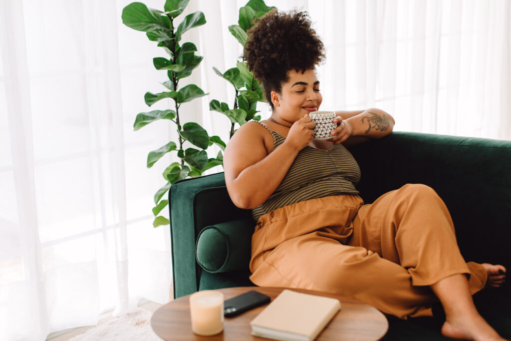Beautiful female having coffee at home. Woman relaxing on sofa and having coffee.