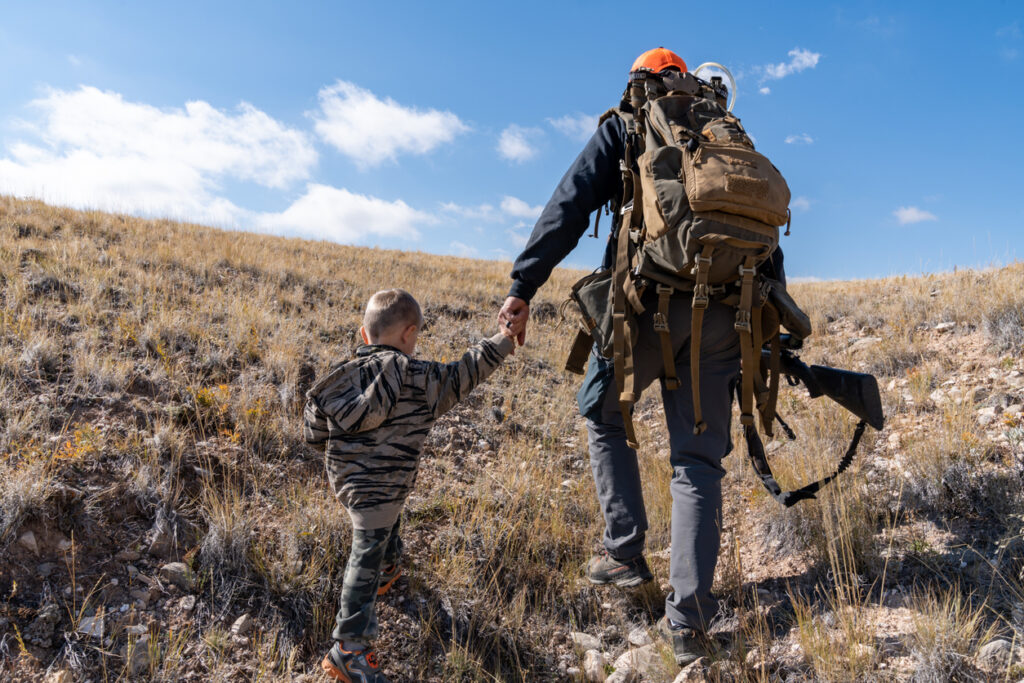 Father and son walk in the sagebrush looking for deer during a child's first hunting trip. Holding hands