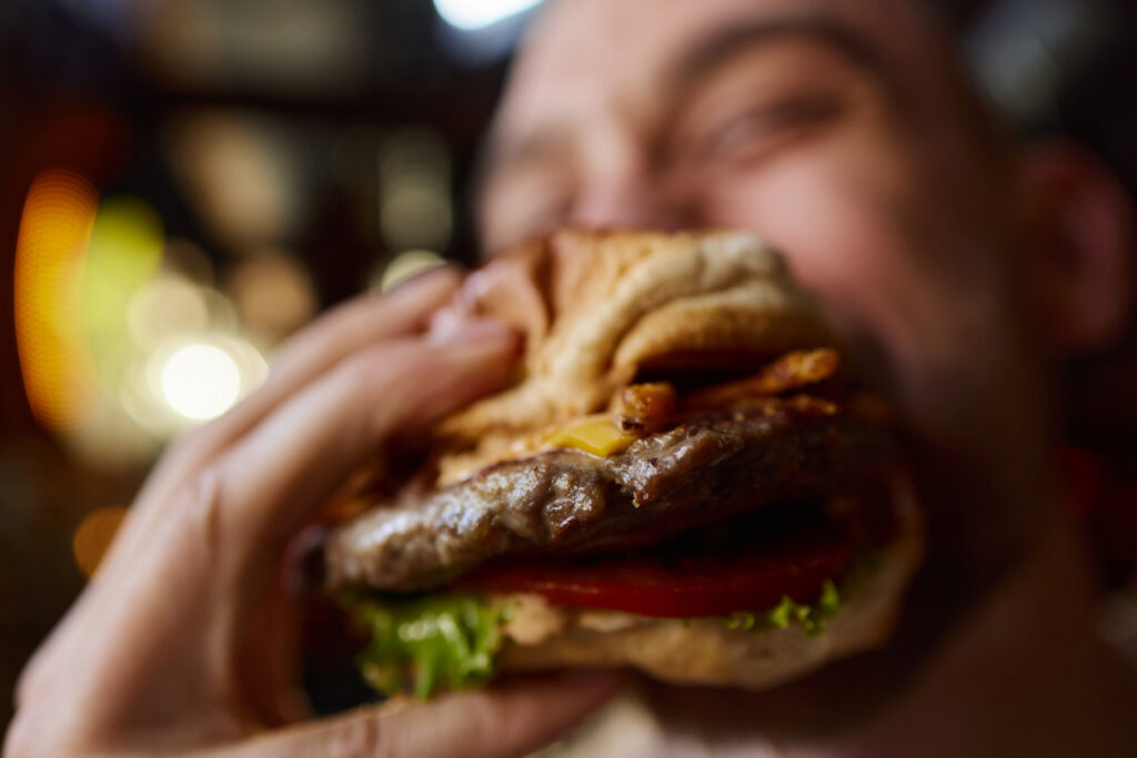 Close up of unrecognizable man eating cheeseburger.