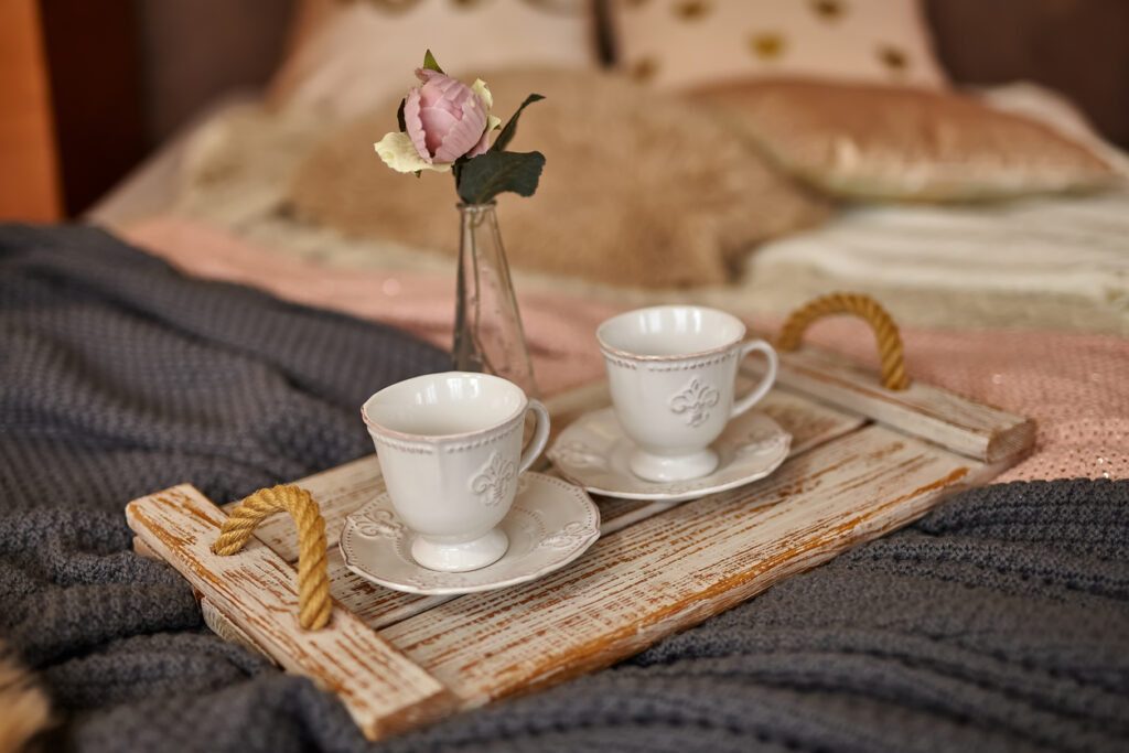Wooden tray of coffee with flower on bed. Romantic Bed with different warm blankets and pillows. Stay Home, quarantine.
