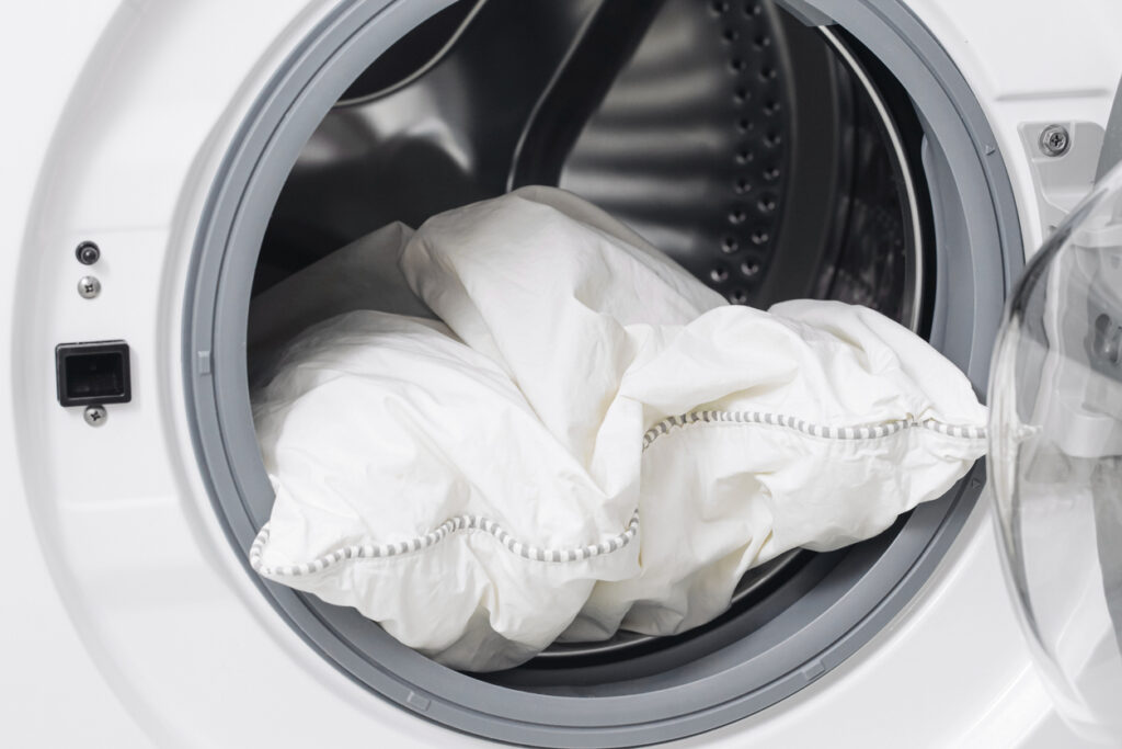 Cleaning bedding in washer. Household hygiene routine. Fresh textile maintenance at home.