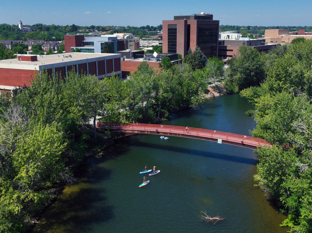 Paddle boarders and people floating the Boise River under a bridge near Boise State University.