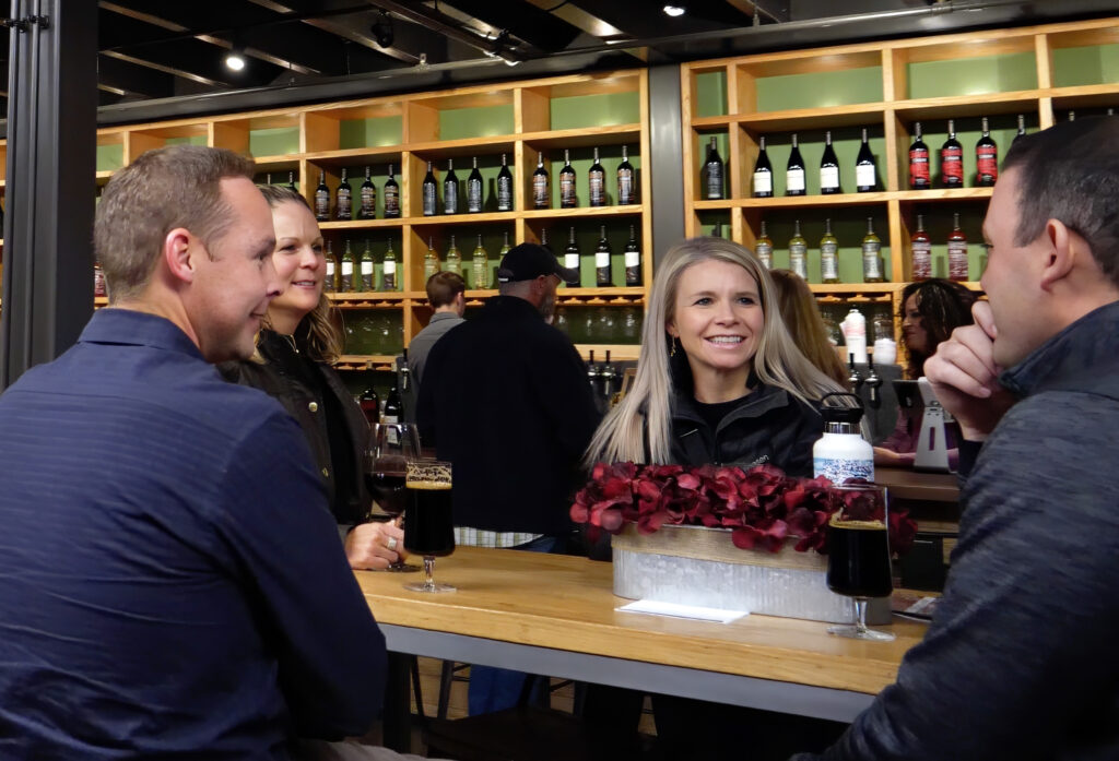 A group of four sitting at a table in Cinder smiling and talking. Cinder Wines urban winery in Garden City, Idaho