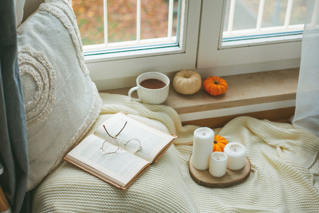 Cup of hot cocoa on a wicker rattan tray near the window, a plaid, a pillow, pumpkins. Cozy. Eco decor for home.